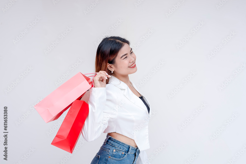 A happy young woman standing sideways while holding her shopping bags to her back. Isolated on a white background. A happy young woman standing sideways while holding her shopping bags to her back. Isolated on a white background.