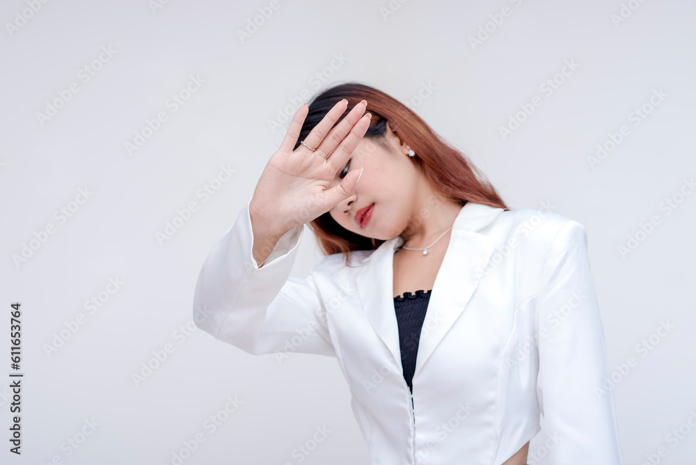 A sad young woman looking down while hiding behind her hand with stop gesture. Isolated on a white background. A sad young woman looking down while hiding behind her hand with stop gesture. Isolated on a white background.