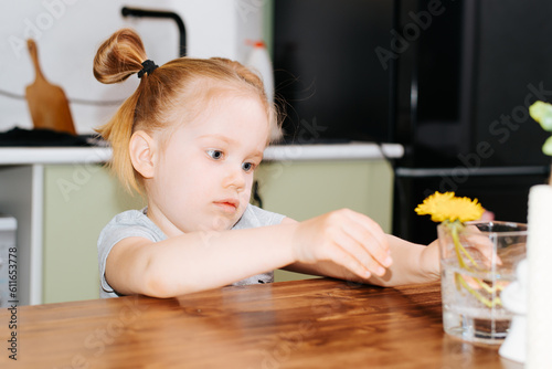 Focused little caucasian girl decorated with flowers table to the kitchen, indoors
