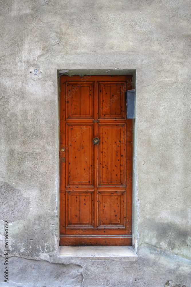 A frontal photo of A vivid wooden door inside a gray plaster door in Italy 