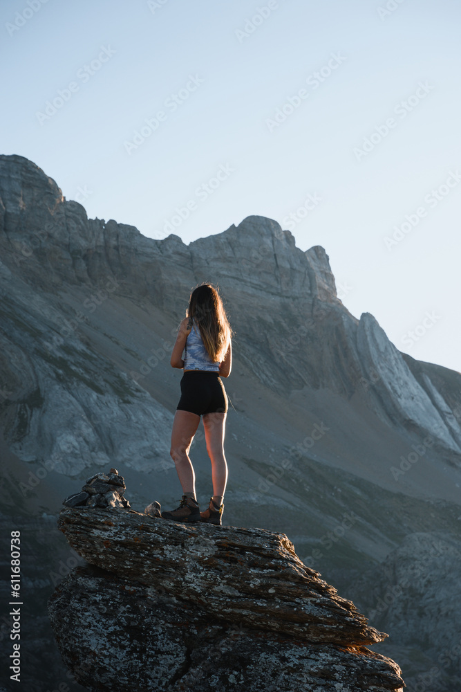 mountaineer girl climbed on a rock at sunset looking at the mountain peaks in the pyrenees of huesca