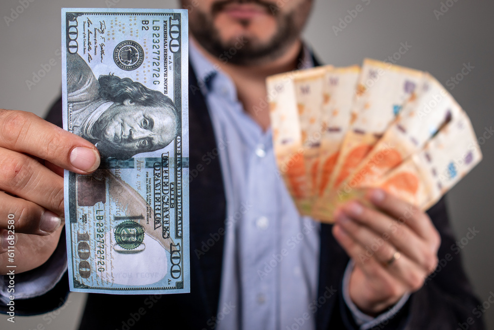 Hombre sosteniendo un billete de 100 dolares y billetes de pesos argentino, en concepto de inflación y devaluación - obrazy, fototapety, plakaty 