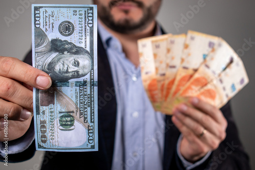 Hombre sosteniendo un billete de 100 dolares y billetes de pesos argentino, en concepto de inflación y devaluación photo