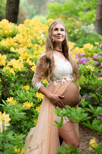 Pregnant woman standing in the rhododendron park. Close up of pregnant belly in blooming nature.