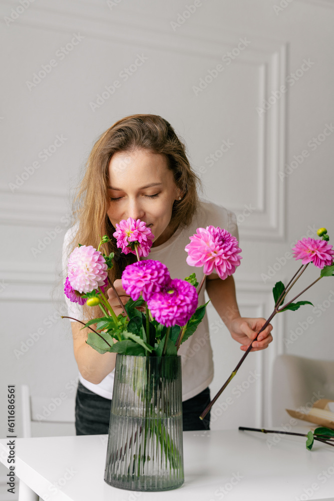 Young female florist sniffing pink dahlias in a vase before arranging them in a bouquet on a white background. Vertical image for your design Young female florist sniffing pink dahlias in a vase before arranging them in a bouquet on a white background. Vertical image for your design