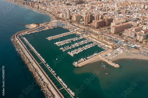 Aerial drone photo of the beautiful beach front of the coastal town of Fuengirola in Malaga Spain Costa Del Sol, showing the harbour with boats in the ocean.