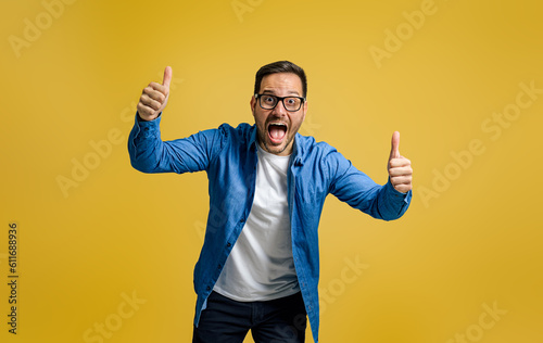 Obraz na płótnie Portrait of exited businessman showing thumbs up and screaming in joy against ye