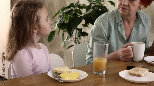 A little blonde girl is having breakfast in the kitchen with an omelette, a sandwich with butter and cheese and orange juice. Delicious and healthy breakfast of natural products for schoolchildren. photo