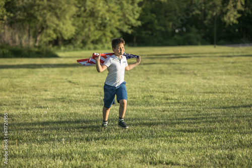 Kid boy celebrating of July, 4 Independence Day of USA . Child running with american flag symbol of United States over wheat field.