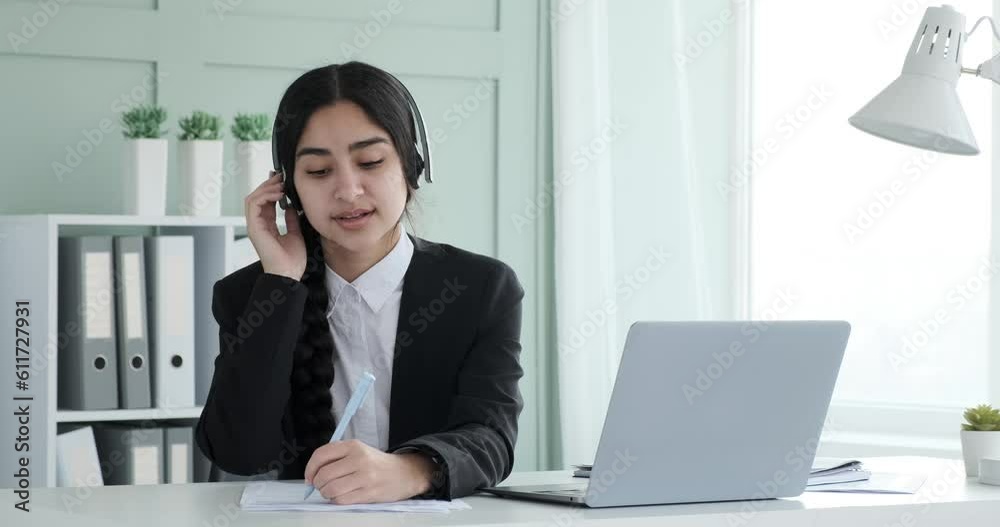 Indian businesswoman, dressed in a black blazer and white shirt, sits in her office wearing headphones. As she listens to music, she seamlessly juggles multiple tasks, including working on paperwork. Indian businesswoman, dressed in a black blazer and white shirt, sits in her office wearing headphones. As she listens to music, she seamlessly juggles multiple tasks, including working on paperwork.