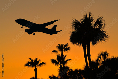 Silhouette of a holiday jet coming into land on a tropical sland at sunset over palm trees. No people. Travel concept