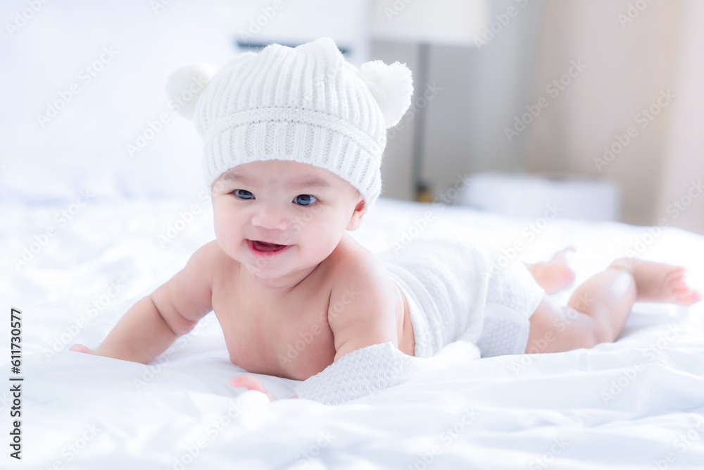 Cute baby in white knitted hat on head and white blanket at waist smilling with happiness emotion after sleep, lie on white bed in bed room in morning. Cute baby in white knitted hat on head and white blanket at waist smilling with happiness emotion after sleep, lie on white bed in bed room in morning.