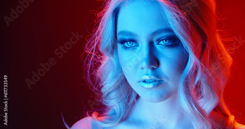 Sensual blonde caucasian girl with glowing makeup giving a tempting look in neon cyberpunk lights - nightlife concept close up portrait shot . Copy Space