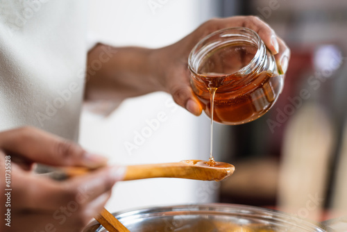 Female hands holding a bowl of bee honey and a wooden spoon. Close up. Elaboration of organic soap based on glycerin.