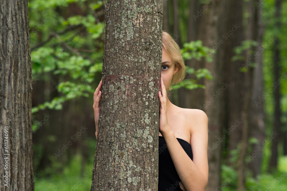 beautiful girl peeking out from behind a tree in the forest beautiful girl peeking out from behind a tree in the forest
