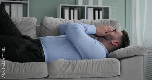 After a hard day at work, a weary Caucasian office worker returns home and plops down on the couch fully clothed. He quickly falls asleep, exhausted from the day's stresses and strains.