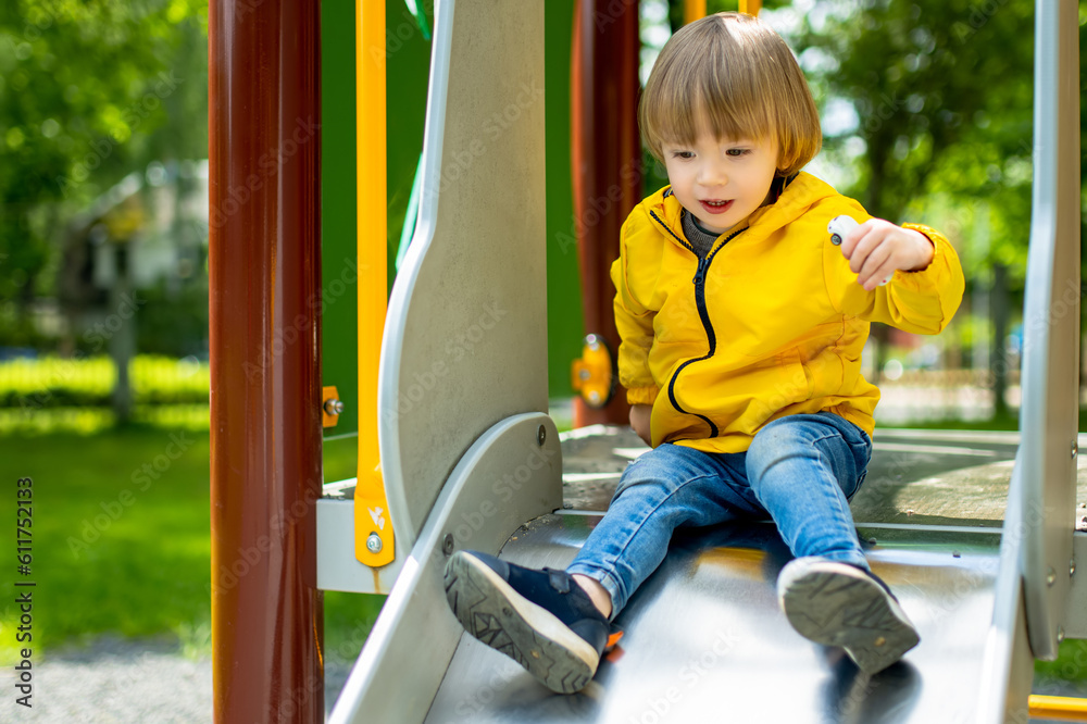 Fototapeta premium Cute toddler boy having fun on a playground outdoors on summer day. Active leisure for kids in summer.