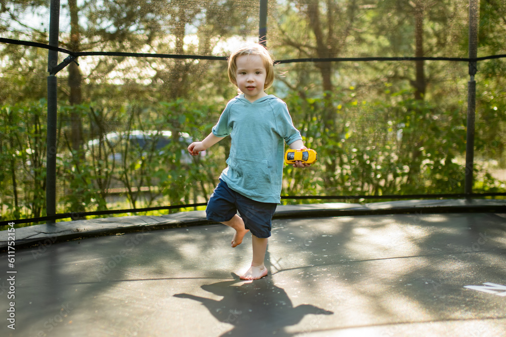 Cute toddler boy jumping on a trampoline in a backyard on warm and sunny summer day. Sports and exercises for children. Cute toddler boy jumping on a trampoline in a backyard on warm and sunny summer day. Sports and exercises for children.