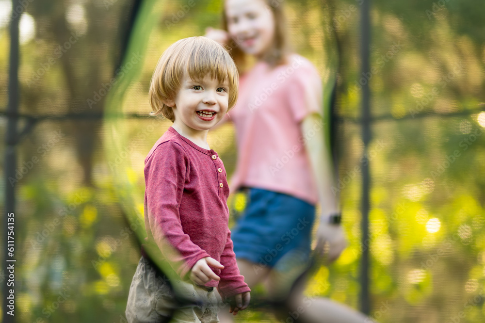 Cute toddler boy and his sister jumping on a trampoline in a backyard. Sports and exercises for children. Cute toddler boy and his sister jumping on a trampoline in a backyard. Sports and exercises for children.