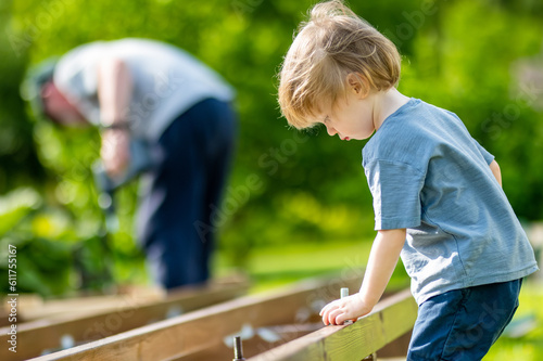 Cute toddler boy helping his grandfather. Senior man working on a project in his garden. © MNStudio