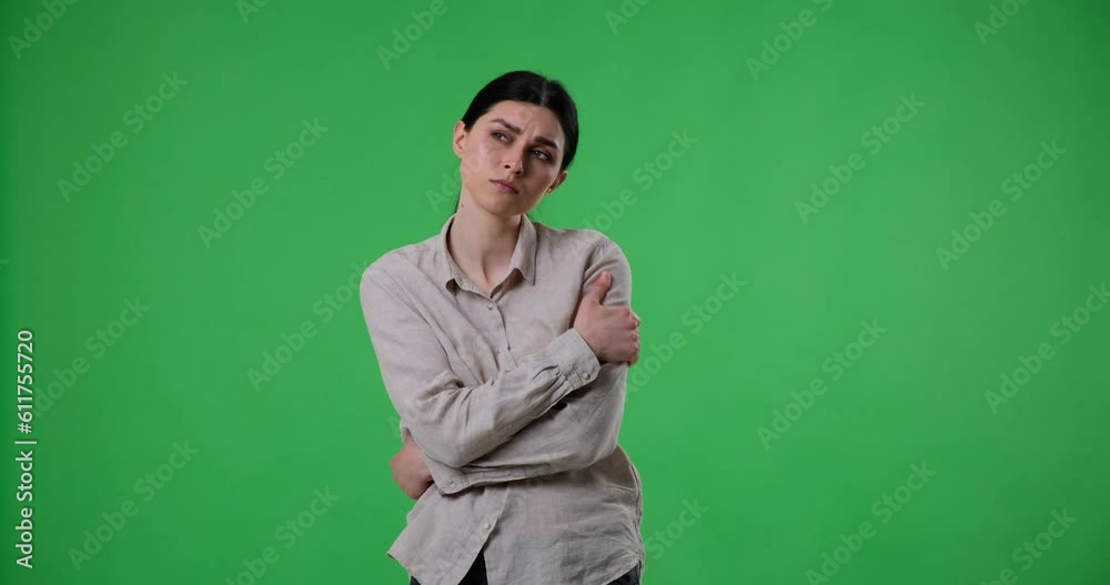 A Caucasian woman stands on a green screen background, hugging herself in a display of loneliness and boredom. Showing loneliness, isolation, sadness. A Caucasian woman stands on a green screen background, hugging herself in a display of loneliness and boredom. Showing loneliness, isolation, sadness.