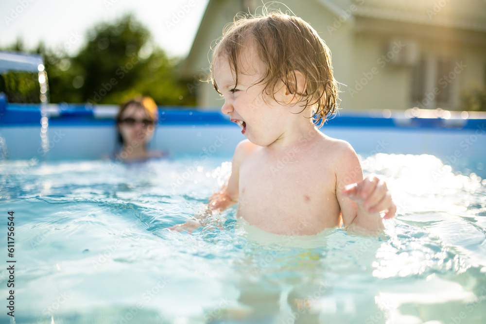 Cuty funny toddler boy and his teenage sister having fun in outdoor pool. Child learning to swim. Kid having fun with water toys. Summer activities for the family with kids.