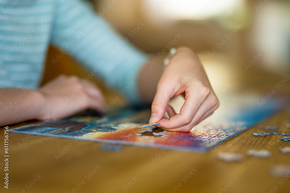 Close-up on woman hand playing puzzles at home. Connecting jigsaw puzzle pieces in a living room table, assembling a jigsaw puzzle.