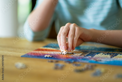 Close-up on woman hand playing puzzles at home. Connecting jigsaw puzzle pieces in a living room table, assembling a jigsaw puzzle.