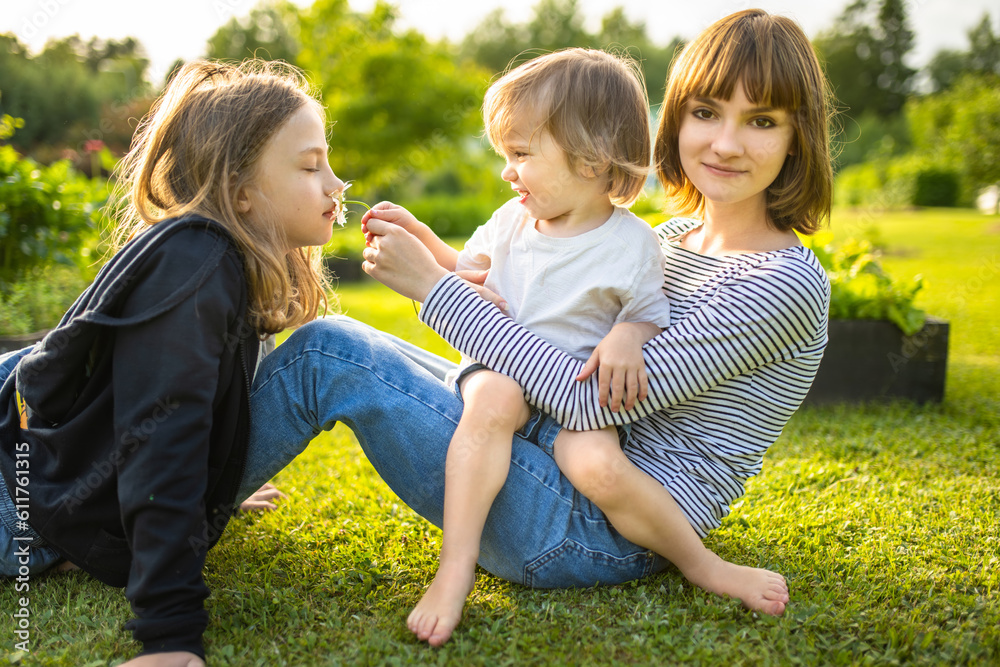 Fototapeta premium Two big sisters and their toddler brother having fun outdoors. Two young girls holding baby boy on summer day. Children with large age gap.