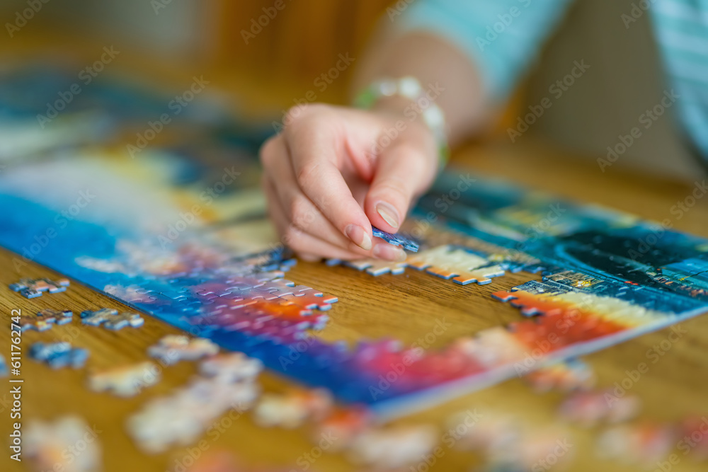 Close-up on woman hand playing puzzles at home. Connecting jigsaw puzzle pieces in a living room table, assembling a jigsaw puzzle. Close-up on woman hand playing puzzles at home. Connecting jigsaw puzzle pieces in a living room table, assembling a jigsaw puzzle.