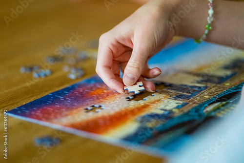 Close-up on woman hand playing puzzles at home. Connecting jigsaw puzzle pieces in a living room table, assembling a jigsaw puzzle.