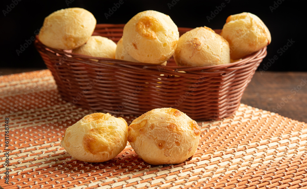 Cheese bread, Basket with cheese bread lying on a wooden woven mat, dark background, selective focus. Cheese bread, Basket with cheese bread lying on a wooden woven mat, dark background, selective focus.