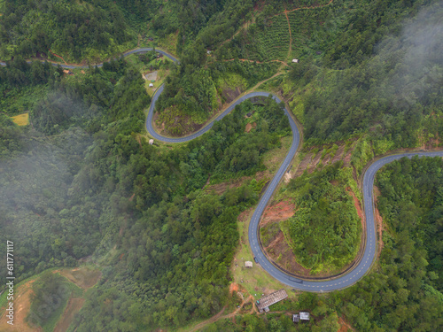 Aerial view of cars driving on curved  zigzag curve road or street on mountain hill with green natural forest trees in rural area of Nan  Thailand. Transportation.