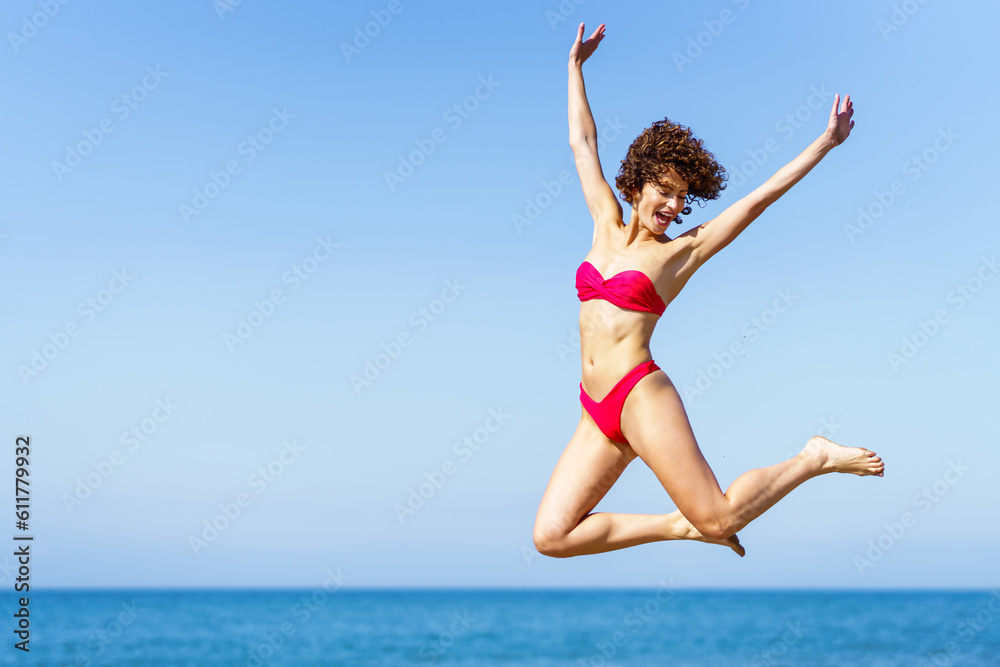 Happy woman in bikini jumping with raised arms