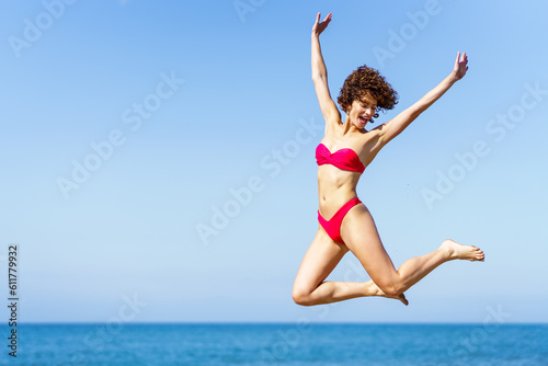 Happy woman in bikini jumping with raised arms