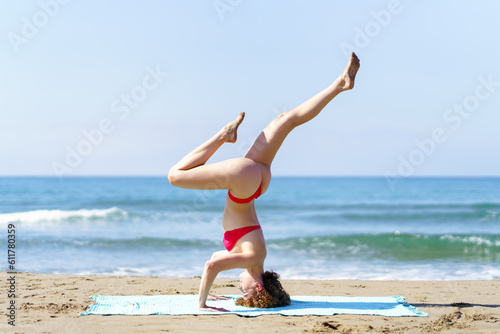 Flexible woman in bikini doing yoga in beach
