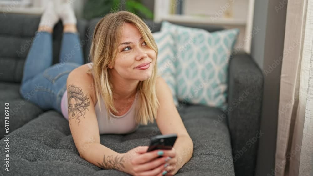 Young blonde woman using smartphone lying on sofa at home Young blonde woman using smartphone lying on sofa at home