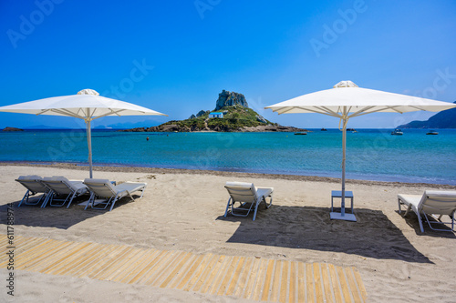 Deck chair and umbrella on beautiful Agios Stefanos Beach in front of paradise Island Kastri- historical ruins and paradise scenery at coast of island Kos, Greece © Simon Dannhauer