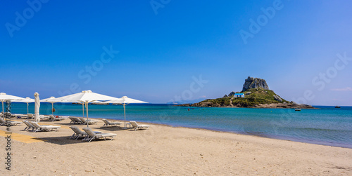 Deck chair and umbrella on beautiful Agios Stefanos Beach in front of paradise Island Kastri- historical ruins and paradise scenery at coast of island Kos  Greece