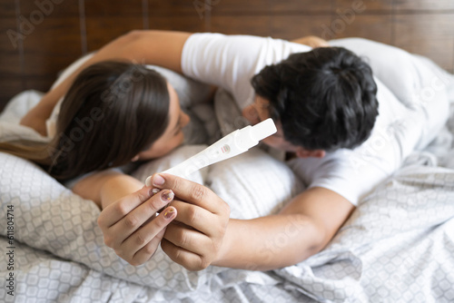 embracing couple hold a positive pregnancy test close-up on the bed