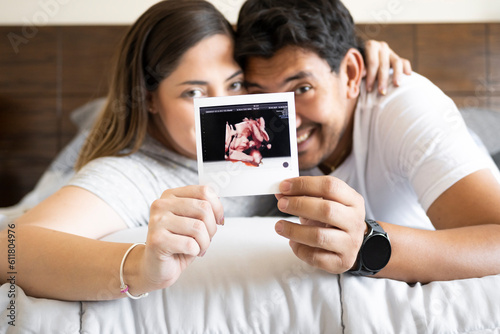 happy married couple look at the camera showing an ultra sound image of their babies