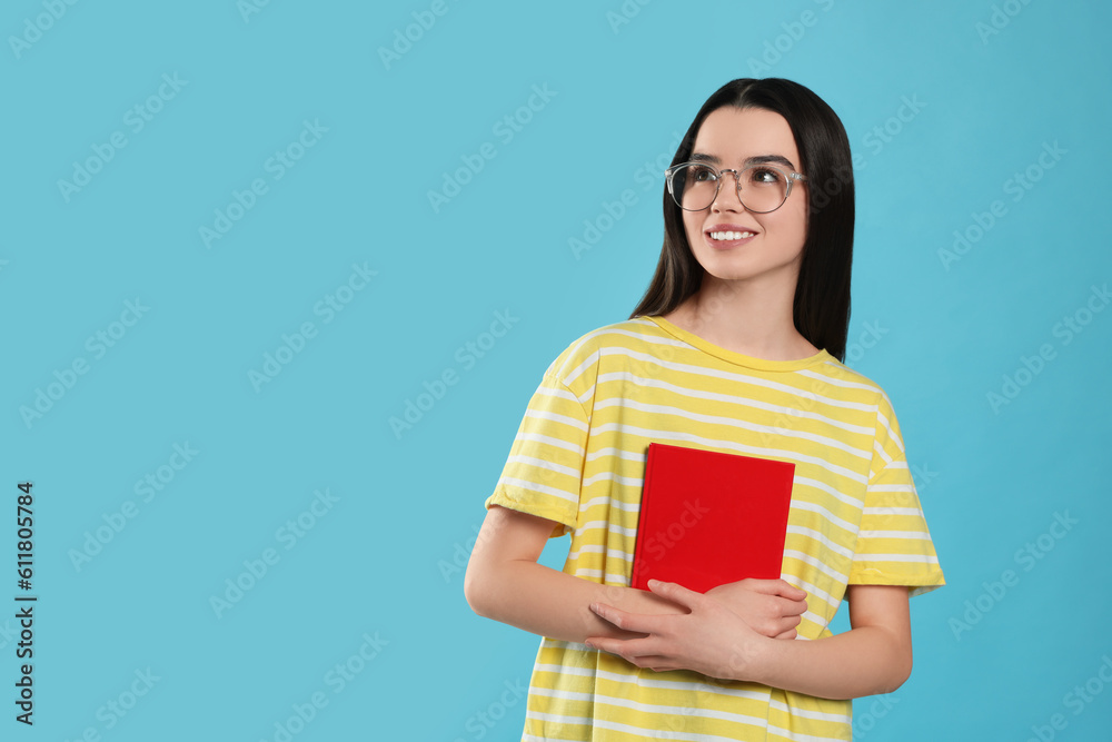 Happy teenage girl in glasses with textbook on light blue background. Space for text Happy teenage girl in glasses with textbook on light blue background. Space for text