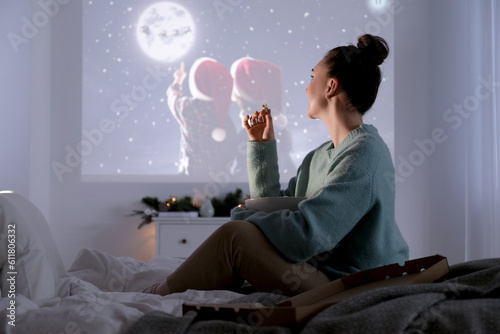 Woman with popcorn watching Christmas movie via video projector at home