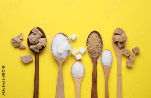 Slika na platnu Spoons with different types of sugar on yellow background, flat lay