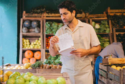 Latin middle-aged man greengrocer taking inventory in a notebook in his organic greengrocer's shop. copy space