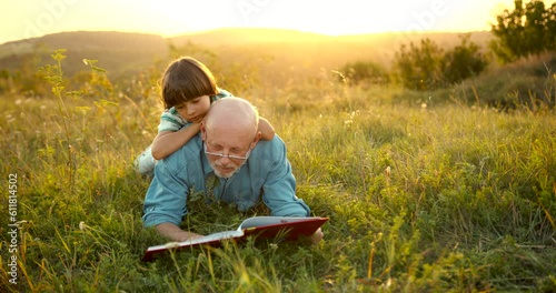 Granfather and grandson laying in grass and reading a book