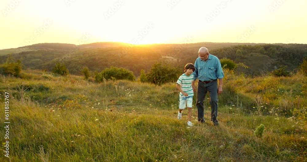 Grandfather and grandson walking at sunset in the field Grandfather and grandson walking at sunset in the field