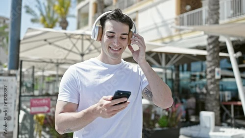 Young hispanic man dancing listening to music on smartphone at coffee shop terrace