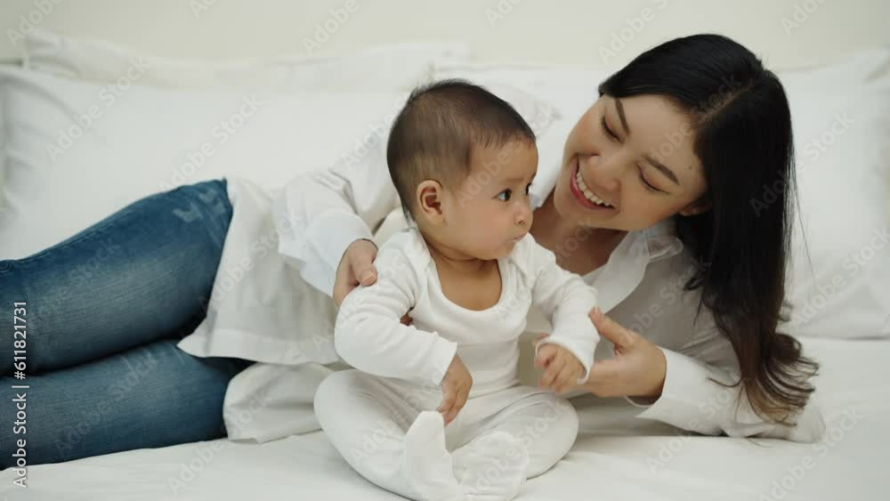 happy mother and her infant baby sitting and playing on a bed happy mother and her infant baby sitting and playing on a bed