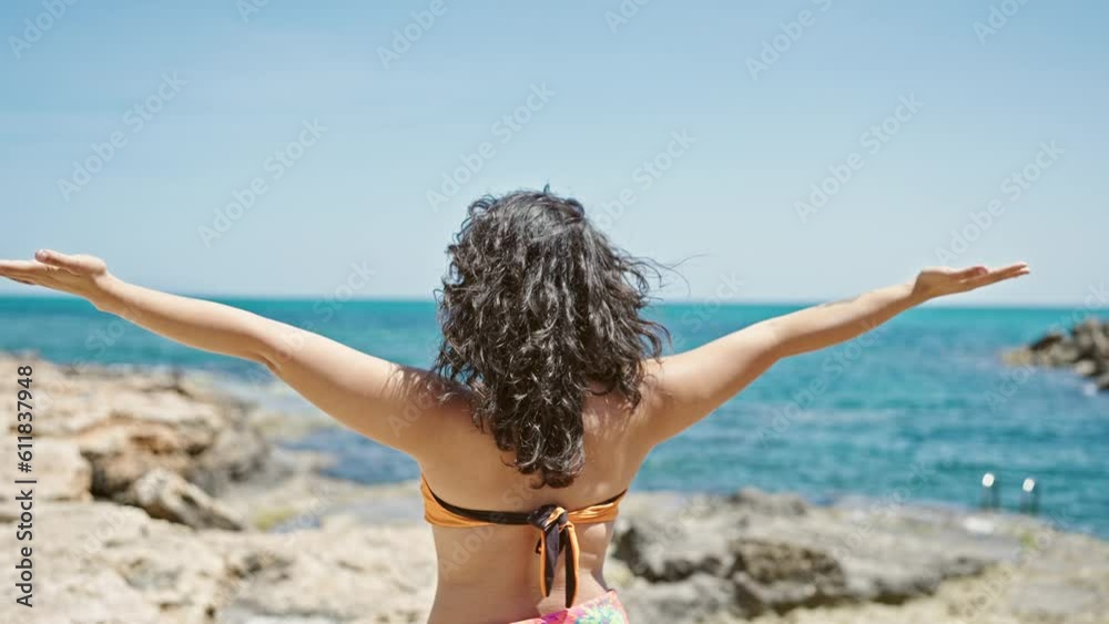 Young beautiful hispanic woman tourist standing backwards stretching arms at beach Young beautiful hispanic woman tourist standing backwards stretching arms at beach